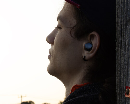 Person is leaning against a wooden pole as they look up at the bright sky.
